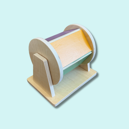 Wooden spinning drum toy with baby safe mirror and pastel panels in purple, yellow, green and blue, designed for Montessori-style baby play